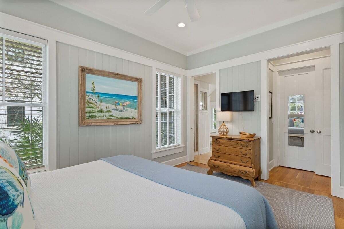 A bedroom with a bed, a dresser, a painting, a television, and a door.