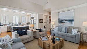 A spacious living area with a kitchen in the background, a large painting on the wall, and a coffee table in the center. - Watersound Resort, Coastal Charm, Walk To Beach! (Inlet Beach)