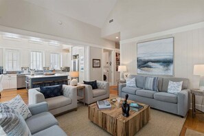 A spacious living area with a kitchen in the background, a large painting on the wall, and a coffee table in the center. - Watersound Resort, Coastal Charm, Walk To Beach! (Inlet Beach)