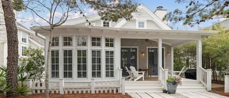 A two-story house with a covered porch, white railings, and a wooden deck.