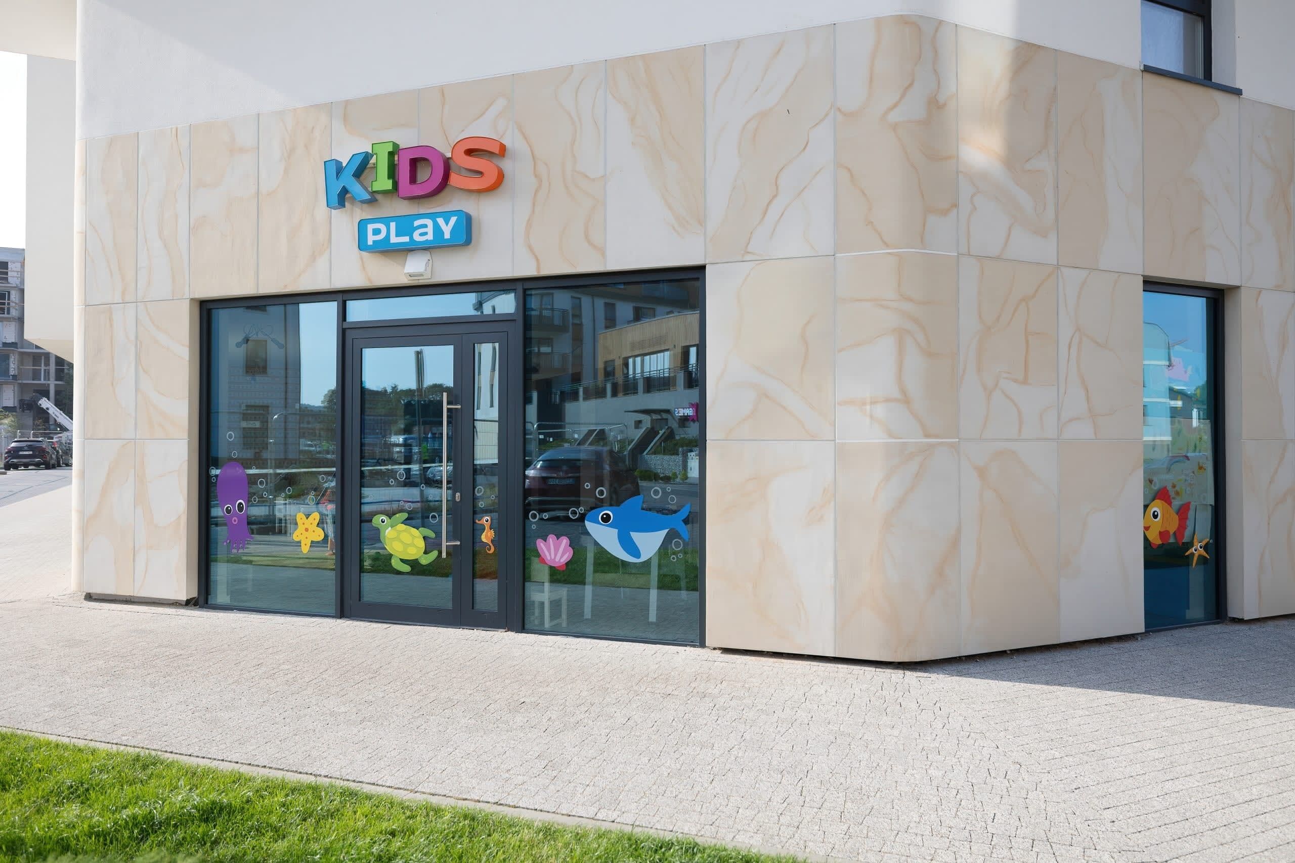 Un bâtiment avec une enseigne indiquant « ESPACE DE JEUX POUR ENFANTS », de grandes fenêtres et une façade recouverte de carreaux.