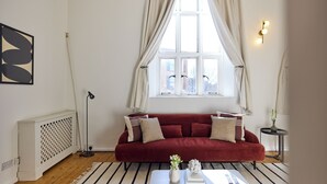 A living room with a red sofa, a white coffee table, a black floor lamp, and a window with curtains. - St Gabriel's Loft Apartment (London)