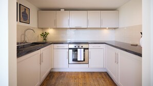 A kitchen with white cabinets, a stainless steel oven, a black countertop, and a wooden floor. - St Gabriel's Loft Apartment (London)