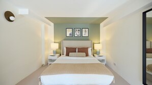 A hotel room with a bed, two bedside tables, a nightstand, a wall-mounted light, and framed artwork. - St Gabriel's Loft Apartment (London)