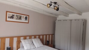 Ett sovrum med en sänggavel i trä, en inramad tavla med hästar, en säng med randigt sänglinne, ett sängbord med en lampa och en gardin.