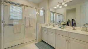 Un baño moderno con ducha envuelta en cristal, un espejo grande y un tocador blanco con armarios.