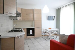 Una cocina moderna con estufa a gas, lavavajillas y armarios de madera. Hay una zona de comedor con mesa y sillas, y un sofá rojo.