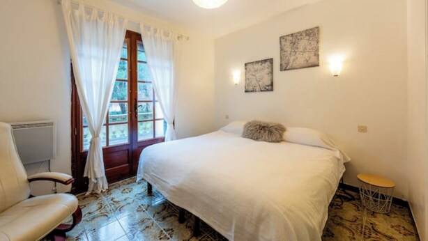 Una camera da letto con un letto, una sedia, un tavolino rotondo e una finestra con tende.