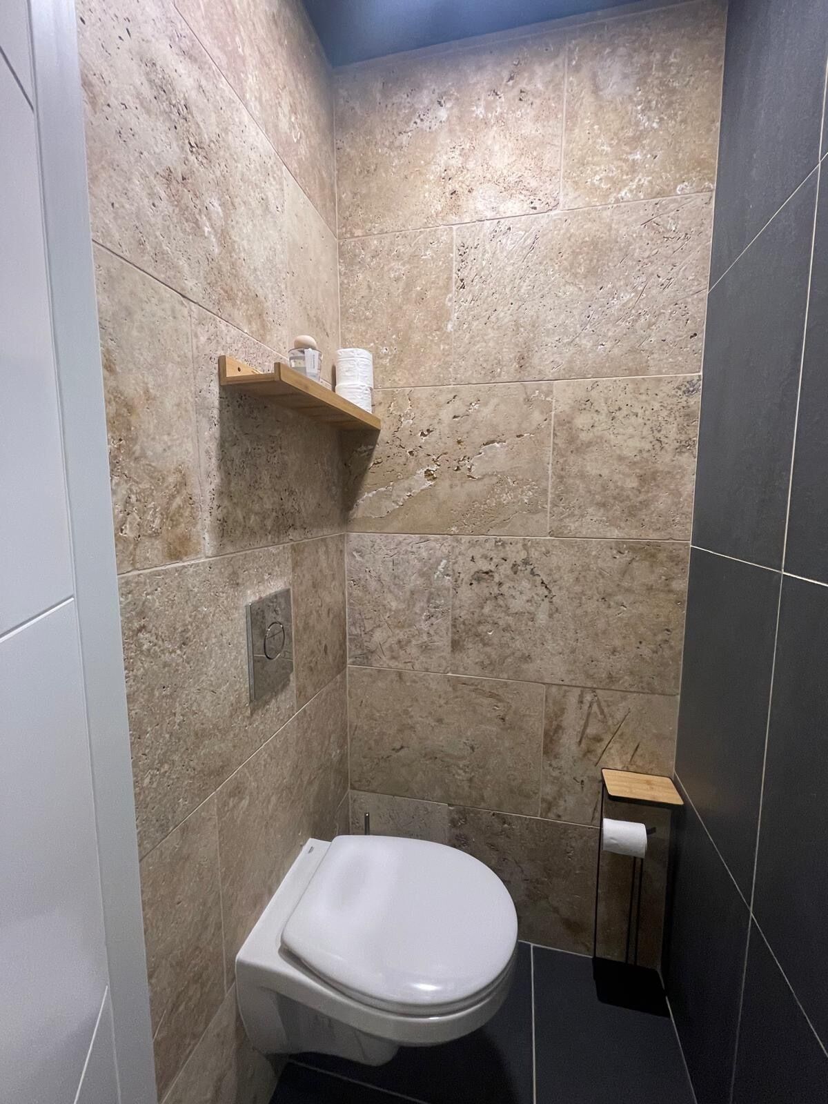 A bathroom with a toilet, a shelf with toiletries, and a small wooden stool.