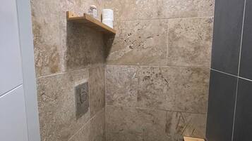 Une salle de bain avec des toilettes, une étagère contenant des articles de toilette et un petit tabouret en bois.