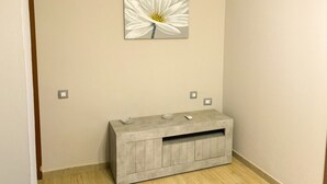 Ein Zimmer mit einer hellen Wand, einem grauen Konsolentisch mit Schublade und einem weißen Blumenbild darüber.