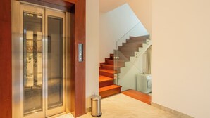 Een modern interieur met een glazen lift, een houten trap en een marmeren vloer.