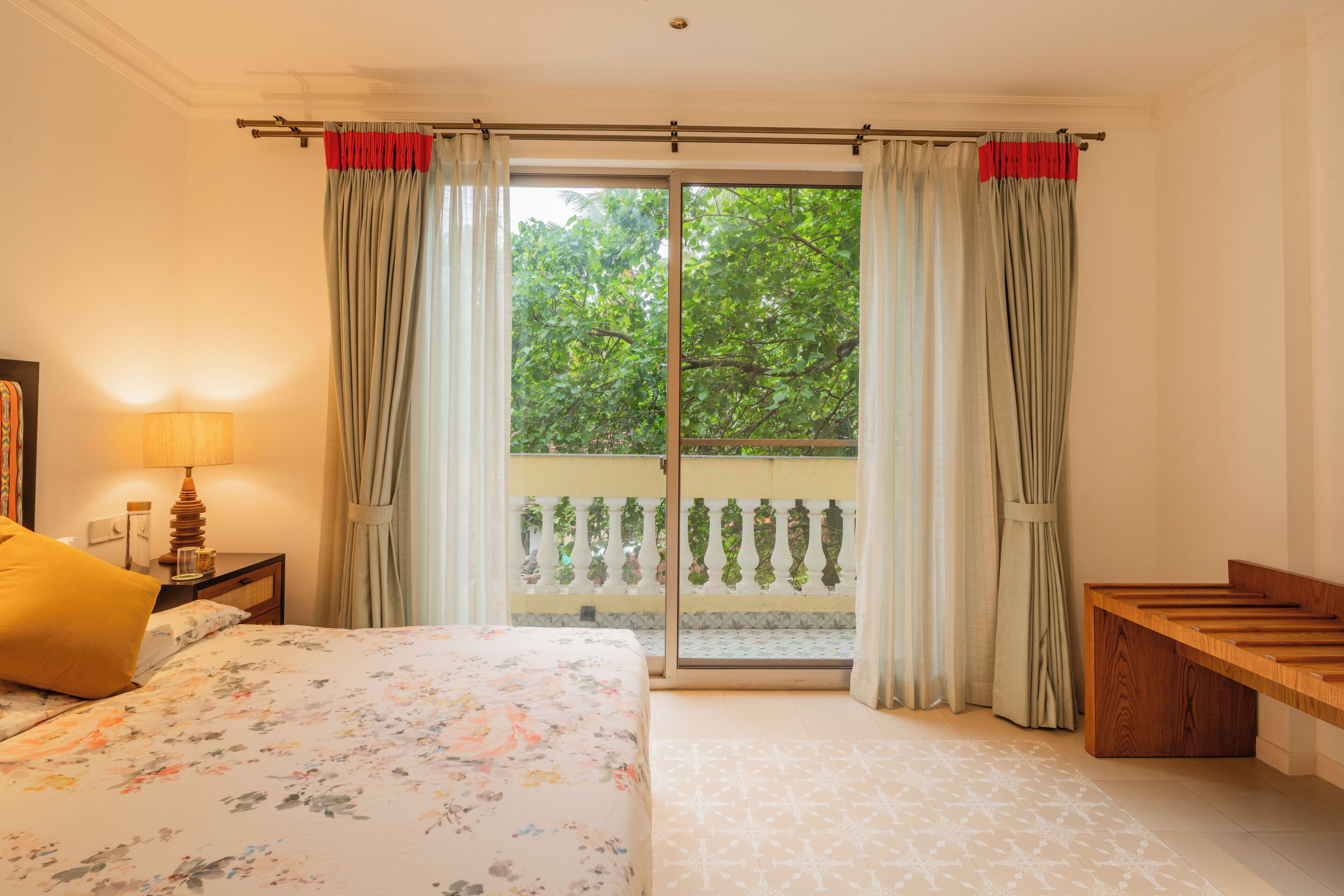 A bedroom with a bed, a bedside table with a lamp, a bench, and a sliding glass door to a balcony.