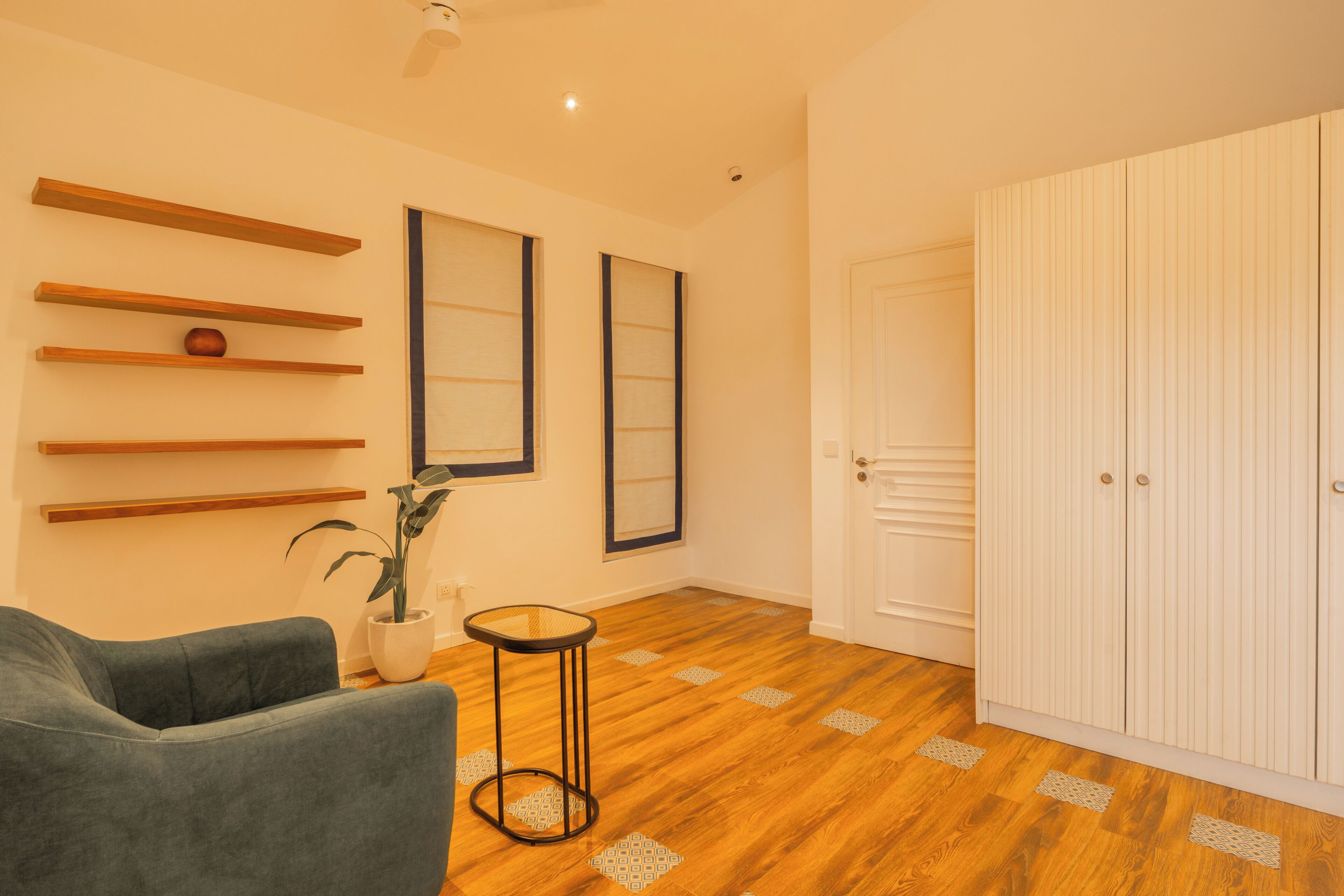 Une pièce avec un canapé gris, des étagères en bois, une plante en pot, une petite table ronde et une armoire blanche.