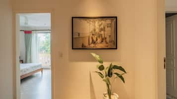 Un pasillo con una obra enmarcada en la pared, una planta en maceta y una cama al fondo.