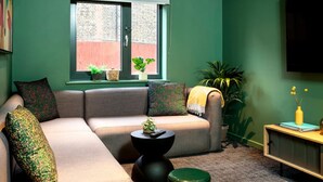 Una sala de estar con sofá, una mesa de centro, una ventana con persianas y una planta en maceta.