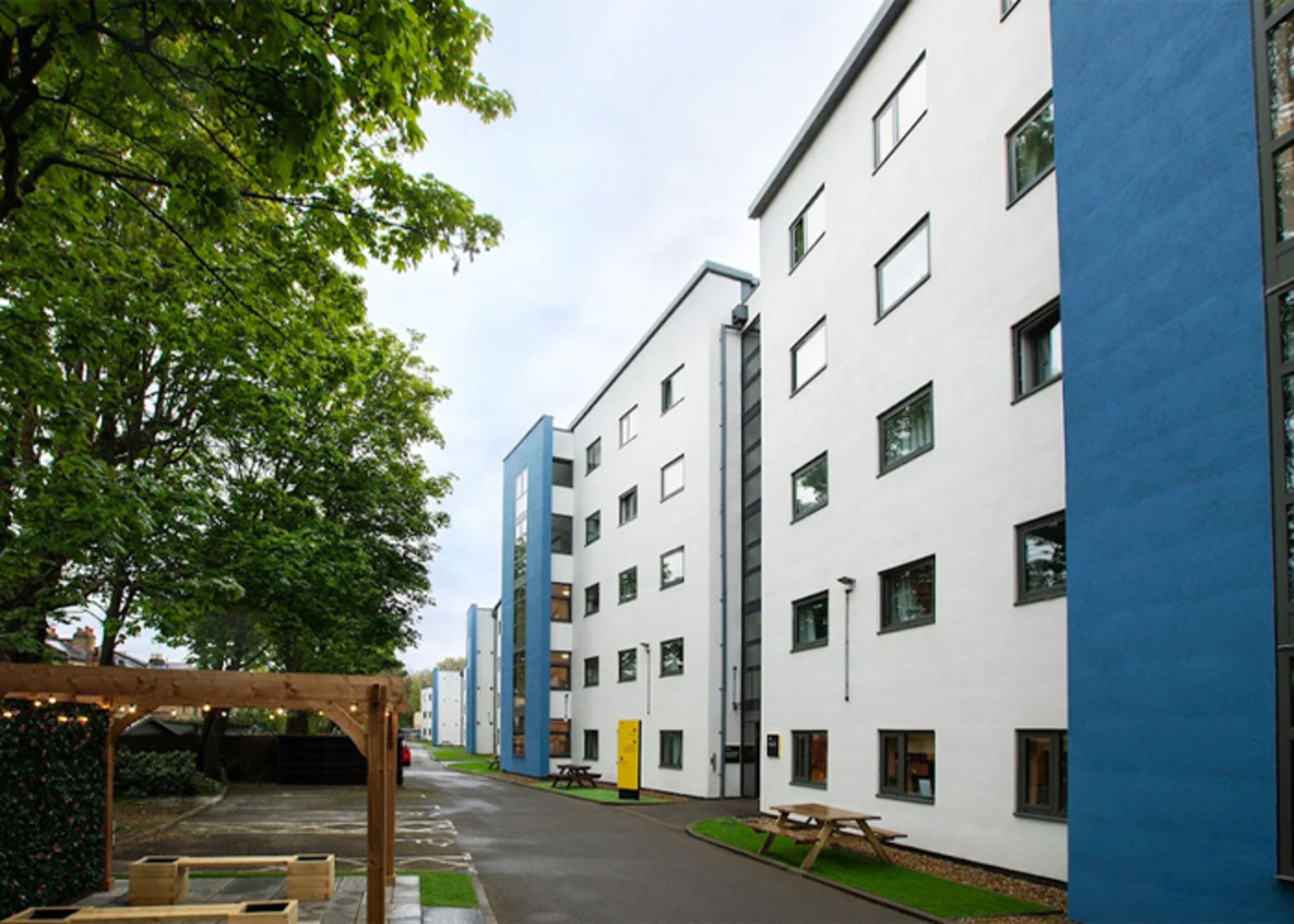 A row of modern buildings with a clear sky, a wooden pergola, and a picnic table.