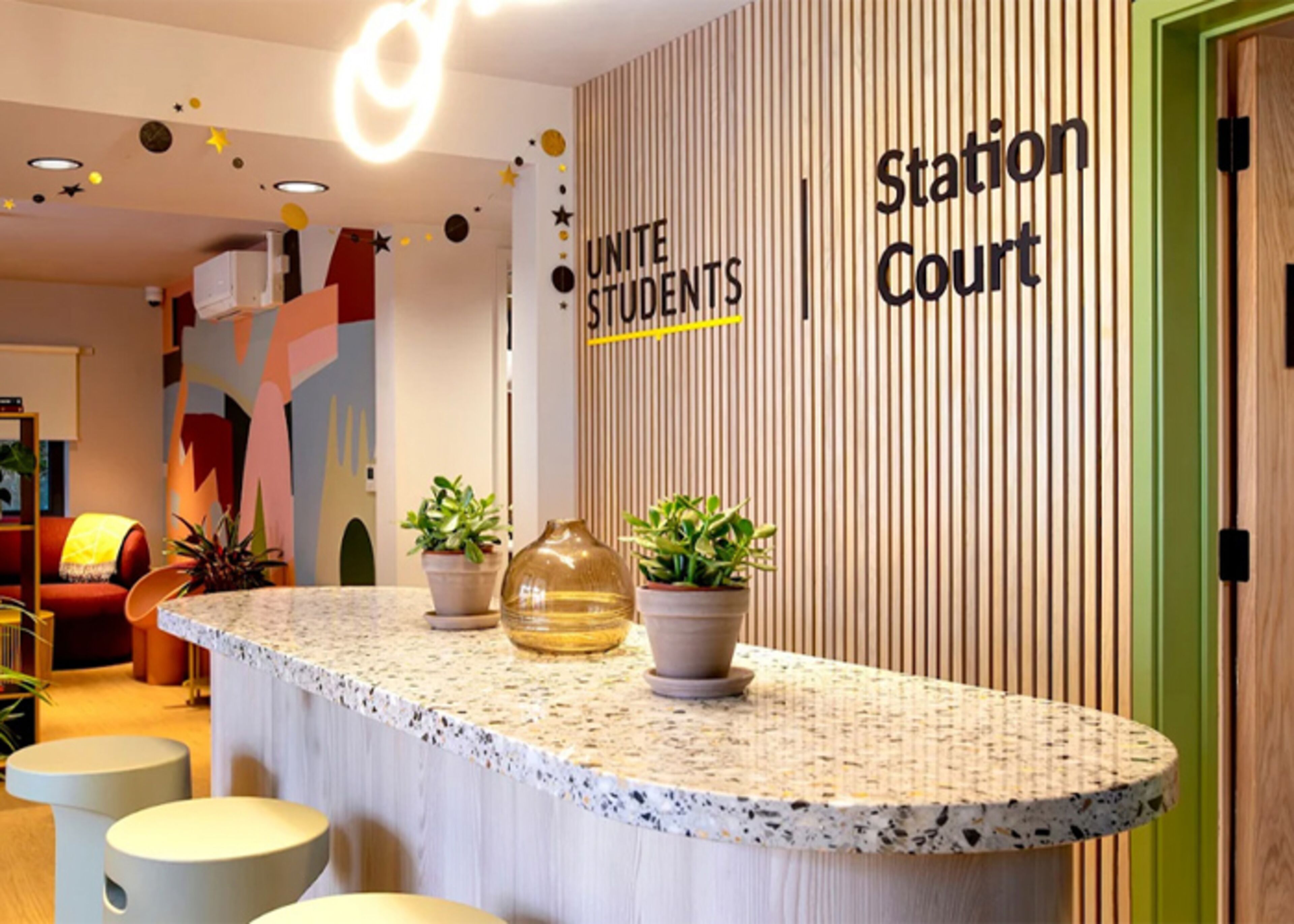 Un'area reception con un bancone, piante in vaso e una parete con la segnaletica 'Station Court'.