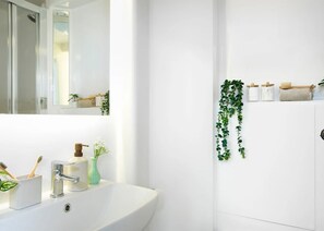 Ein Badezimmer mit einem weißen Waschbecken, einem Spiegel, einer Dusche und einem Wandregal mit Toilettenartikeln.