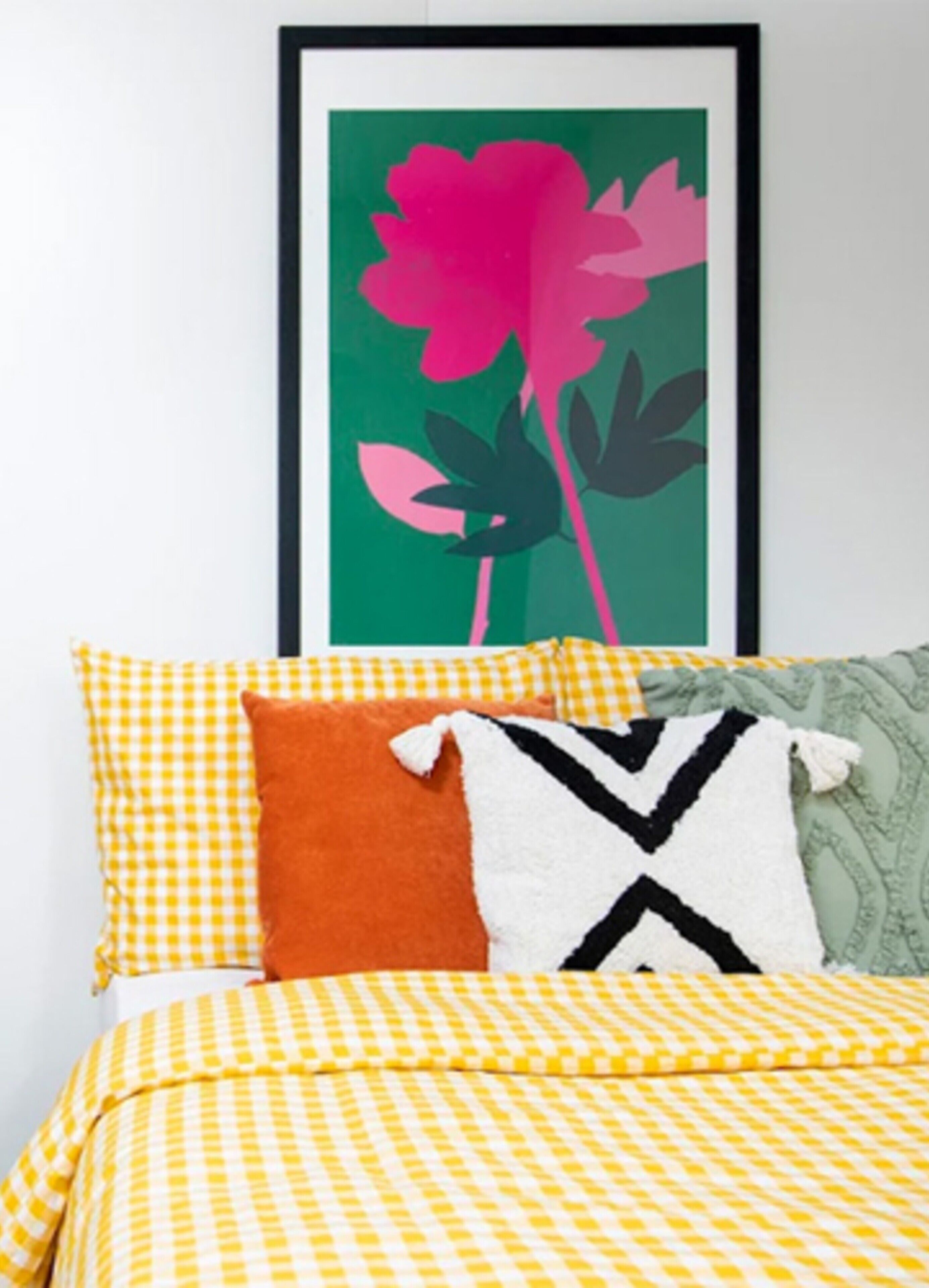 A bed with a yellow checkered bedspread, a white pillow with a black pattern, an orange pillow, and a green patterned pillow.