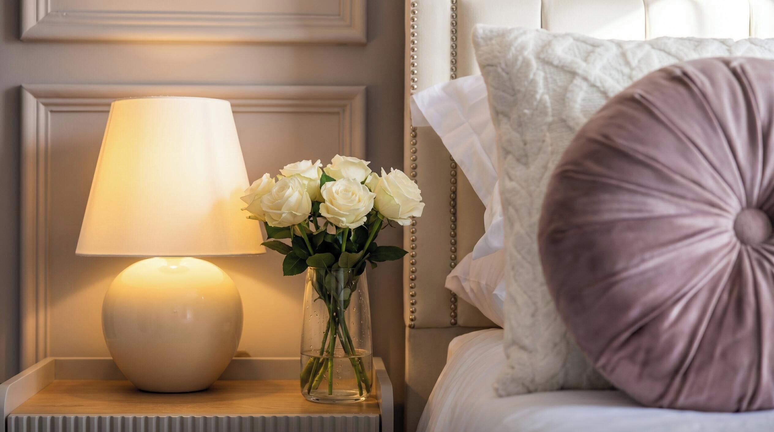 Une table de chevet avec une lampe et un vase de roses blanches.