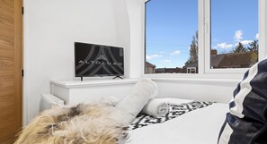 Ein Schlafzimmer mit einem Bett, einem Fernseher auf einem Schrank und einem Fenster mit Blick auf Häuser.
