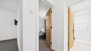 Un pasillo con una cama y un armario, un interruptor de luz y una puerta que da a un baño con baldosas de mármol.