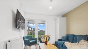 Una sala de estar con un sofá azul, un sillón azul, una mesa de centro de madera y un televisor montado en la pared.