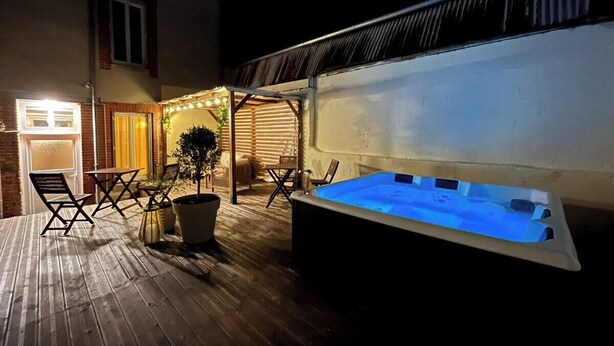 Ein Außenbereich mit Whirlpool, Holzboden, Sitzgelegenheiten und einer überdachten Terrasse.