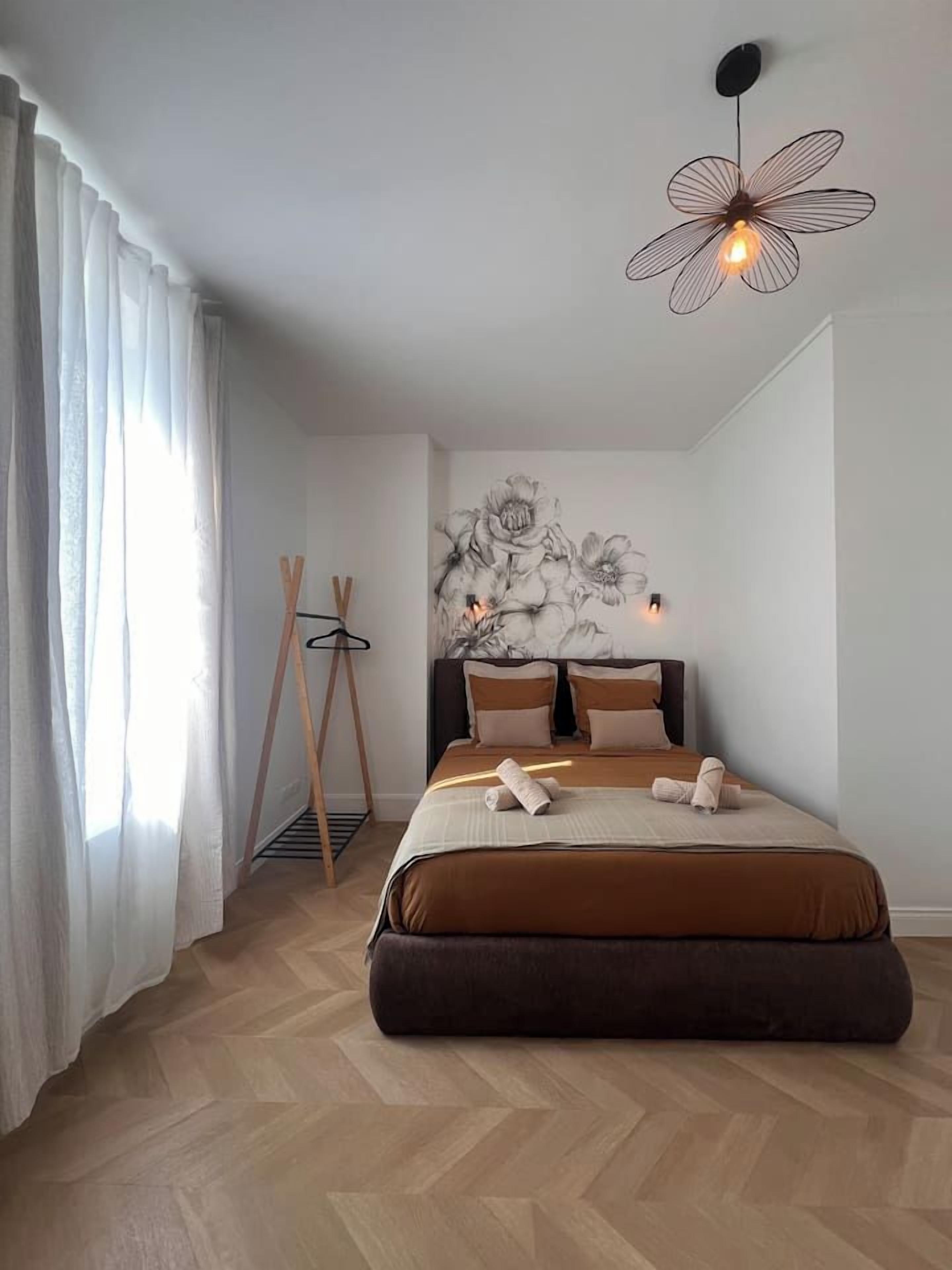 A bedroom with a large bed, a hanging light fixture, and a wall-mounted artwork.