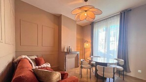 Ein Wohnzimmer mit einer Couch, einem Kamin, einem Esstisch mit Stühlen und einem großen Fenster mit Vorhängen.