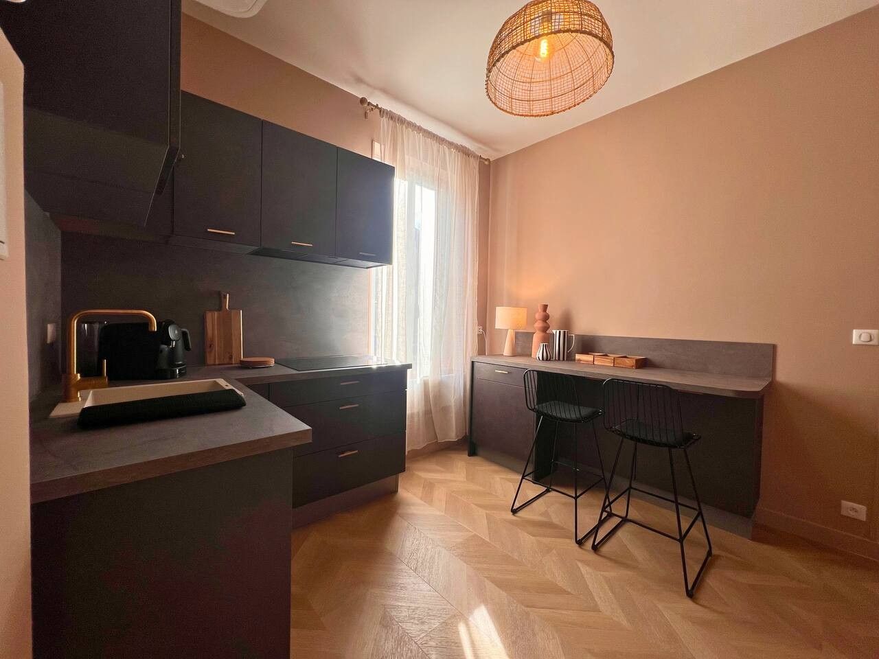 A compact kitchen with dark cabinetry, a coffee machine, and a bar area with stools.