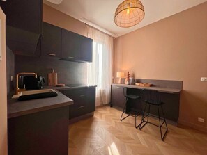 Una cocina compacta con muebles oscuros, una cafetera y una barra con taburetes.