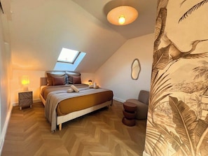 Un dormitorio con cama, mesita de noche, silla, espejo en la pared y luz de techo.