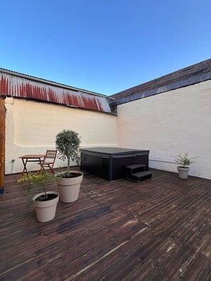 Una terraza de madera con una mesa, sillas, un árbol pequeño y un sofá exterior negro.