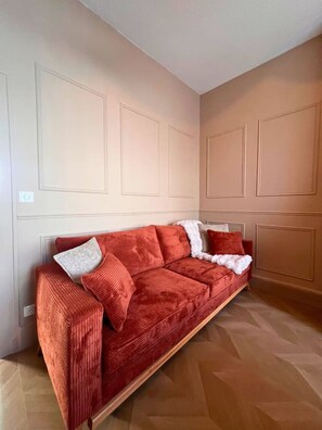 Un canapé rouge avec des coussins blancs et gris, dans une pièce aux murs de couleur beige et aux boiseries en bois.