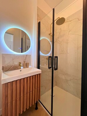 Ein modernes Badezimmer mit einer Duschkabine aus Glas, einem Waschtisch mit Marmorplatte und runder LED-Beleuchtung.