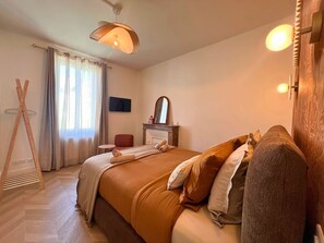 Un dormitorio con cama, mesita de noche, silla, escalera de madera y ventana con cortinas.