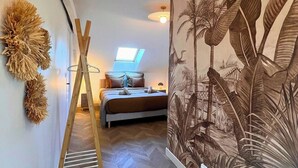 Ein Schlafzimmer mit einem Bett, einer Holzleiter, einem Wandregal und einem großflächigen Wandgemälde.
