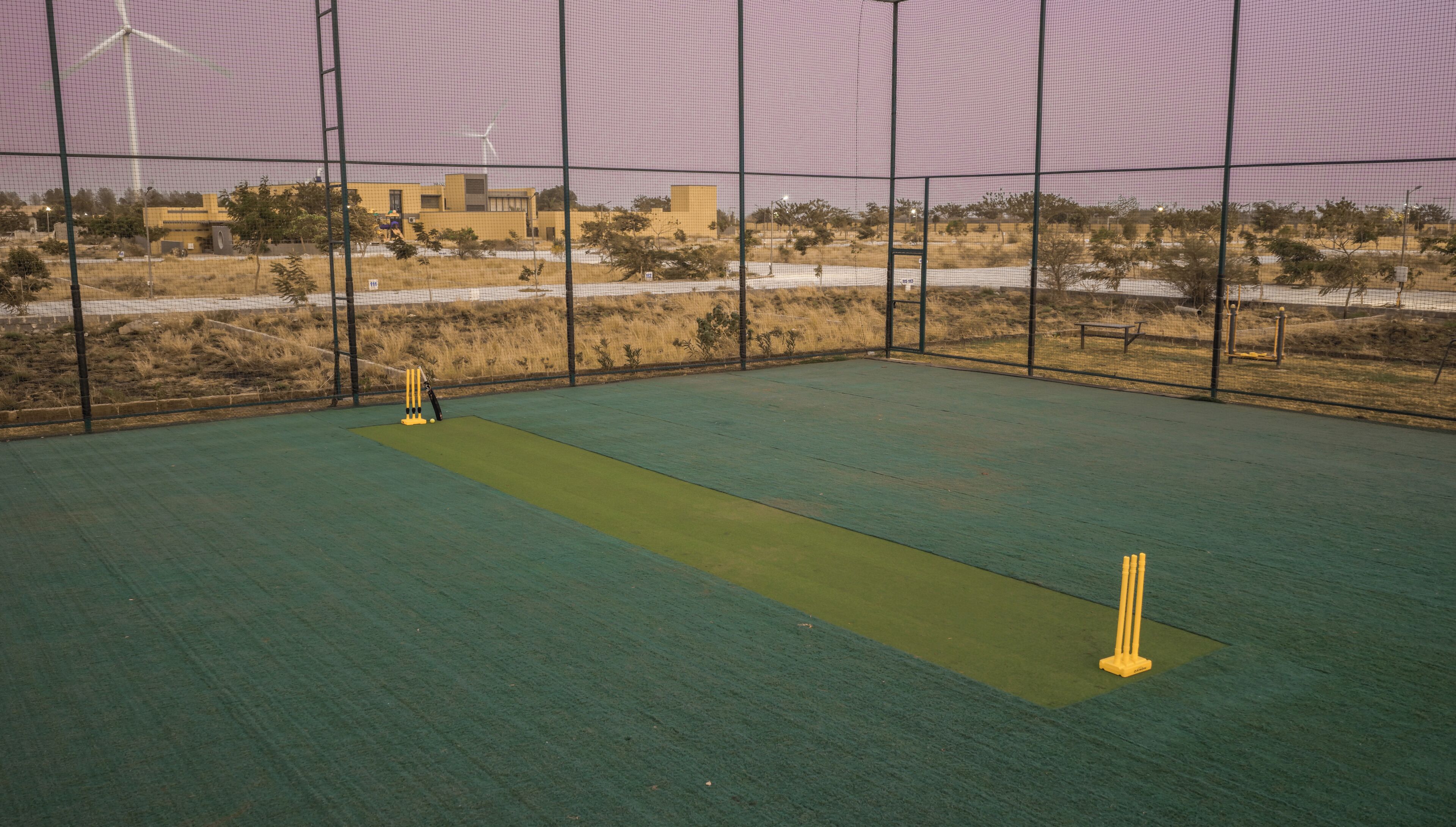 An indoor cricket pitch with a netted enclosure, a wicket, and stumps.