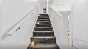 Uma escadaria com corrimão, degraus carpetados e uma vela acesa na base.