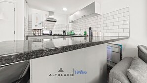Uma cozinha moderna com paredes azulejadas brancas, bancada de granito e um termoacumulador visível.