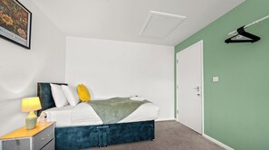 Un dormitorio con cama, mesita de noche, lámpara y un cuadro en la pared.