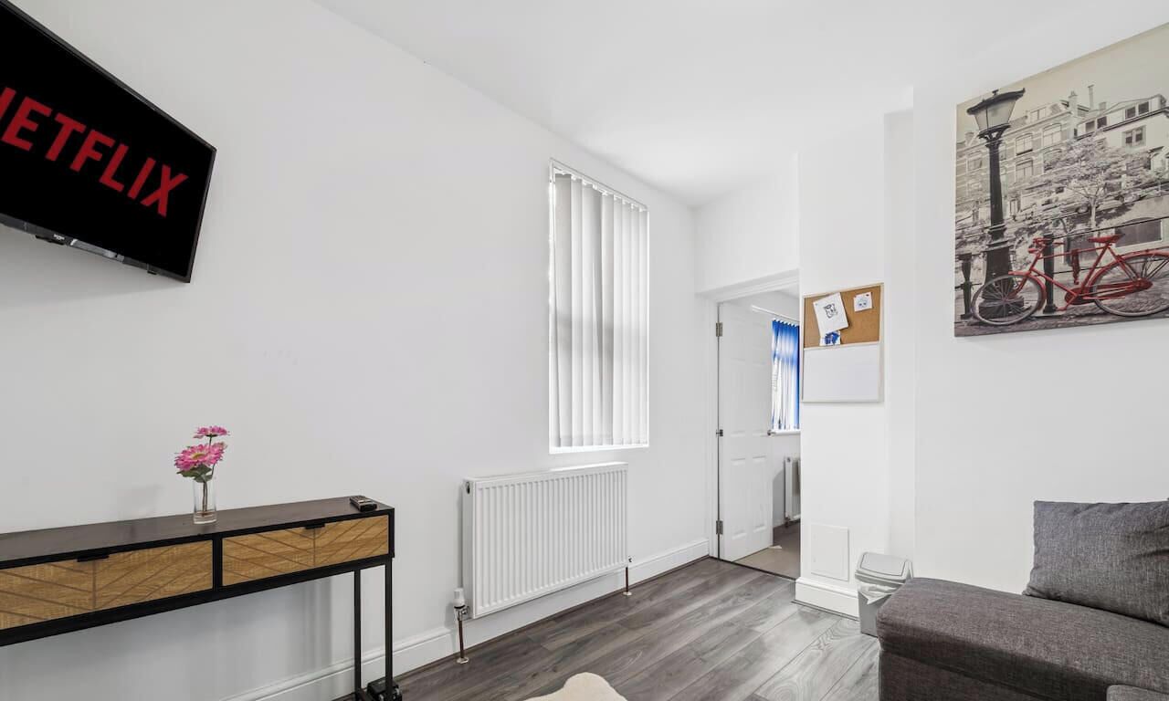 Un salon moderne avec un téléviseur à écran plat, un radiateur, une console sur laquelle est posé un vase, et un tableau accroché au mur.