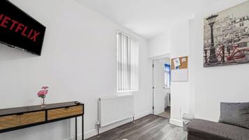 Un salon moderne avec un téléviseur à écran plat, un radiateur, une console sur laquelle est posé un vase, et un tableau accroché au mur.
