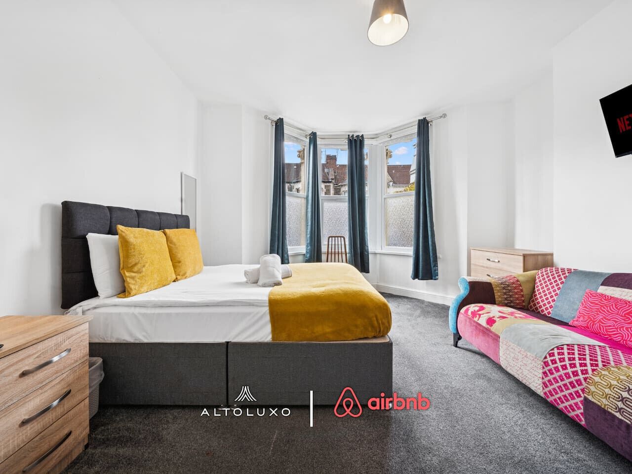 Une chambre moderne avec un lit, un canapé, une commode en bois et une fenêtre avec des rideaux.
