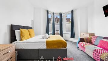 Une chambre moderne avec un lit, un canapé, une commode en bois et une fenêtre avec des rideaux.