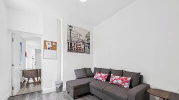 Un salon moderne avec un canapé d’angle gris, un coin repas comprenant une table et des chaises, et une œuvre d’art fixée au mur représentant un vélo.
