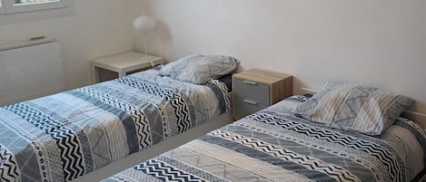 Makuuhuoneessa on kaksi sänkyä, yöpöytä, lamppu, ikkuna ja seinälle ripustettu autokuva.