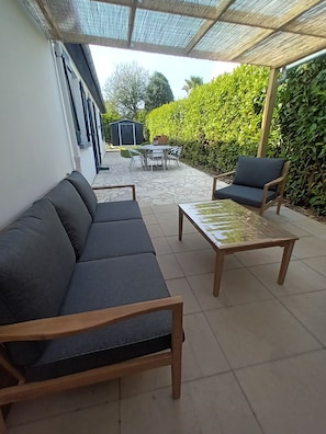A patio with a sofa, a table, and a chair, a covered area, and a hedge. - Single-storey house with enclosed garden (Crozon)
